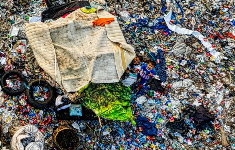 Aerial view of massive rubbish dump full of plastic with children looking up at the camera.. 